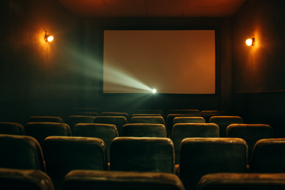 Ruang bioskop independen kecil dengan kursi beludru dan sorot proyektor ke layar kosong